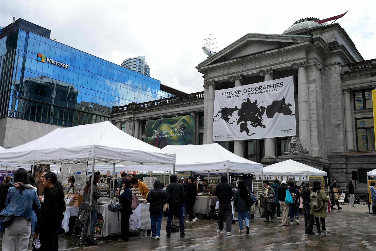 バンクーバー美術館の正面。VANCOUVER ART GALLERYの看板とライオン像、手前に白いテントが並ぶ市場の様子