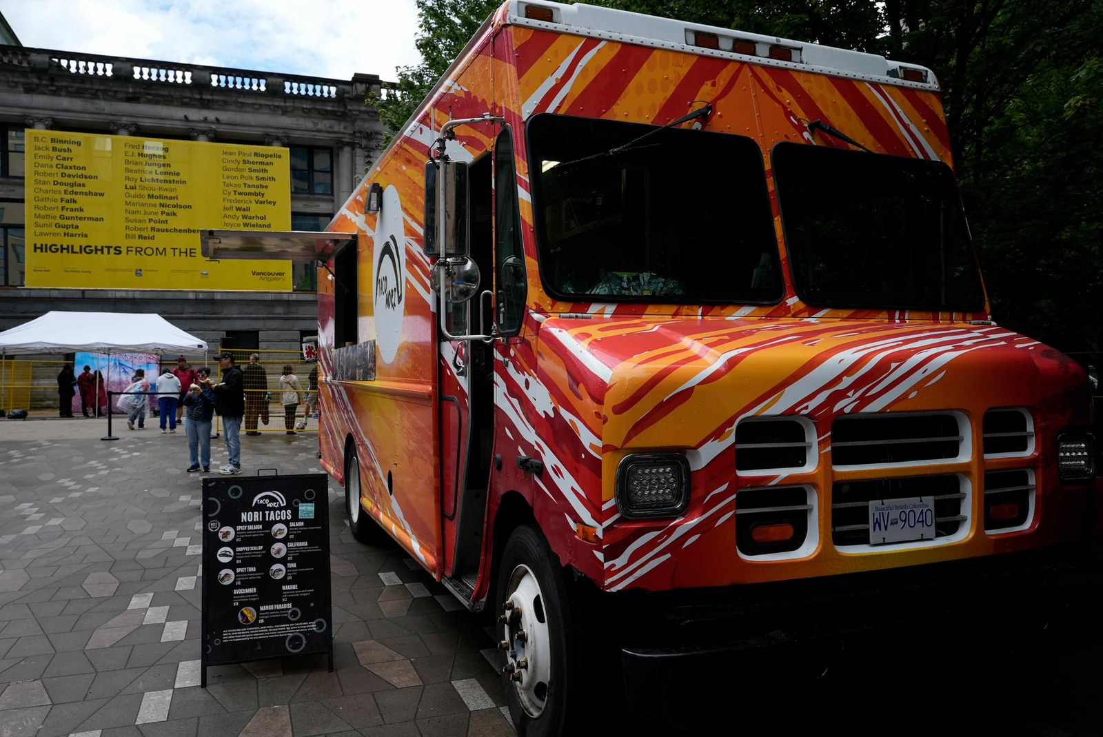 オレンジと赤に塗られたキッチンカー「NORI TACOS」。メニューボードにはスパイシーサーモンやツナなどの巻き寿司タコスが並ぶ