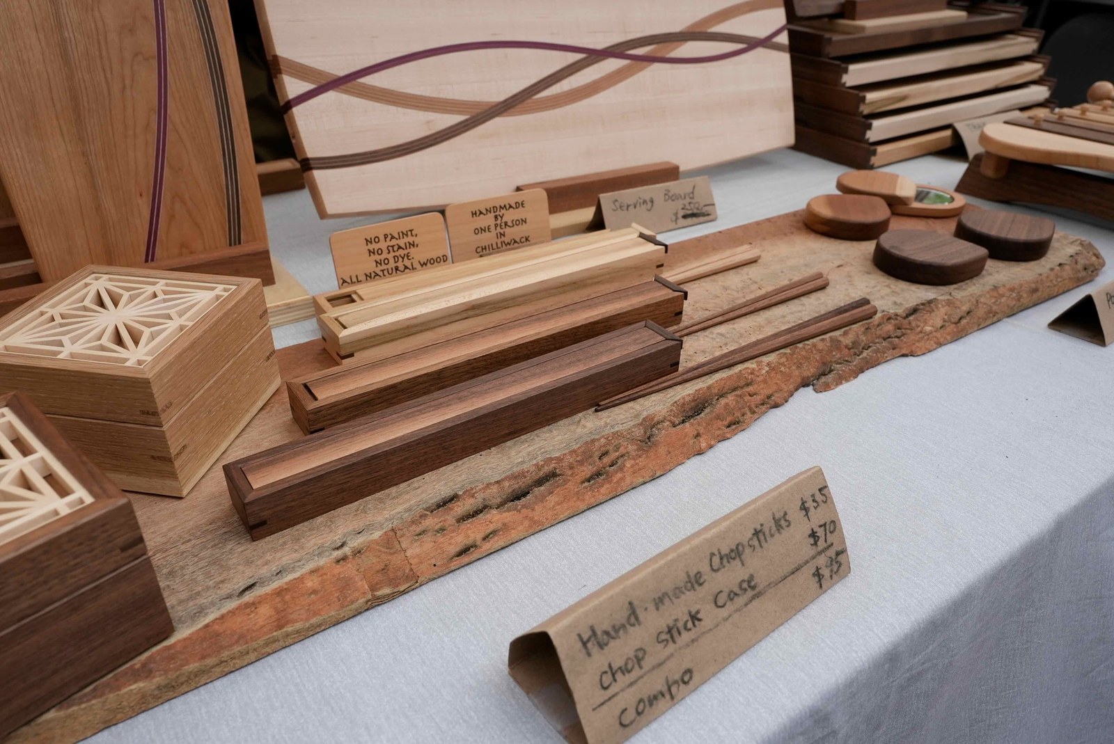 木工作品の展示。木製の柵越しに、赤いジャケットの職人さんが作業する様子と、来場者の姿