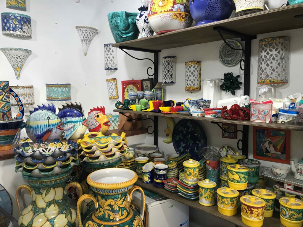 陶器店の棚。魚やニワトリ、月の顔、レモン柄の壺など多彩なモチーフが並ぶ