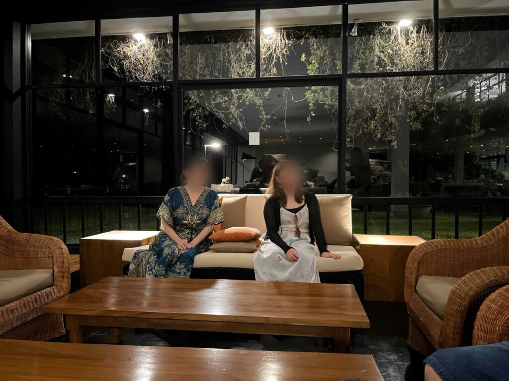 夜のラウンジ。ガラス越しに植栽が照らされ、ソファでくつろぐ宿泊客